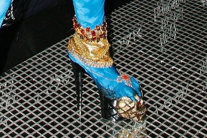 Details of Heidi Klum's blue platform boots featuring gold jewelry and long toenails clawing at a golden skull