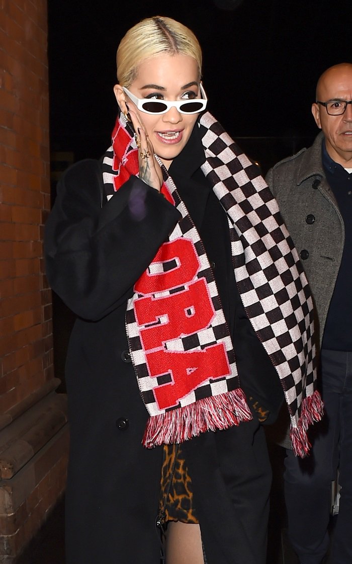 Rita Ora wears a fringed checkerboard scarf that says 'HOUSE OF FUCKING HOLLAND'