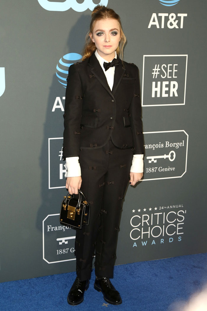 Elsie Fisher wearing a Thom Browne Pre-Fall 2019 bow-embellished suit, bow-adorned patent-leather oxford shoes, and carrying a calfskin 'Mrs. Thom' tiny bag