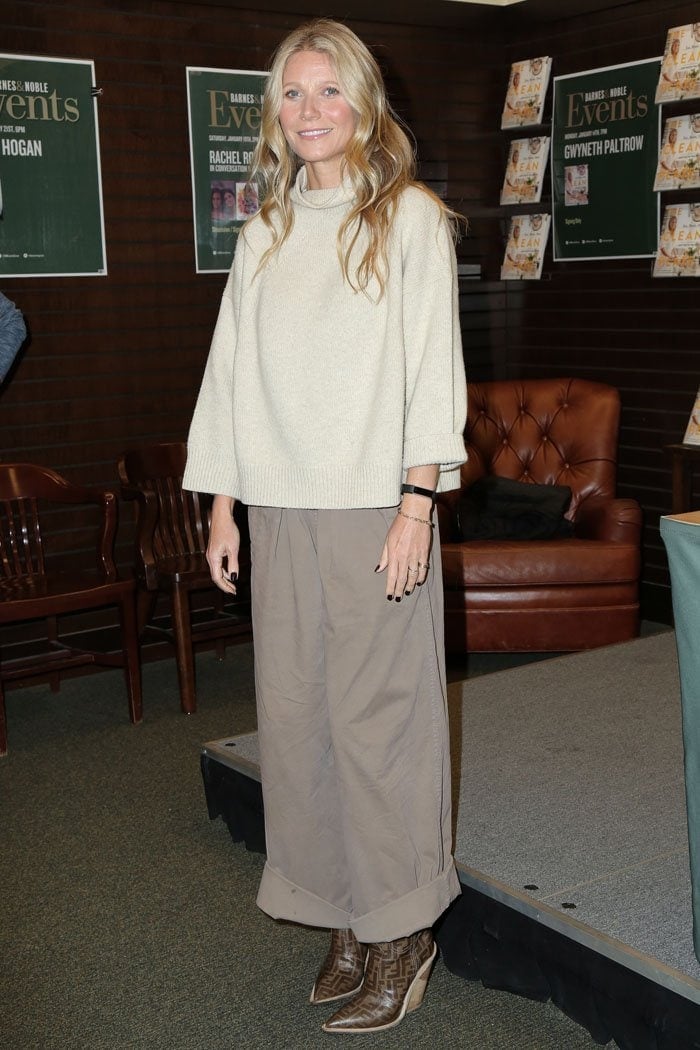 Gwyneth Paltrow in a frumpy brown outfit consisting of a loose beige turtleneck sweater, wide-leg pleat-front pants, and Fendi logo-print cowboy boots