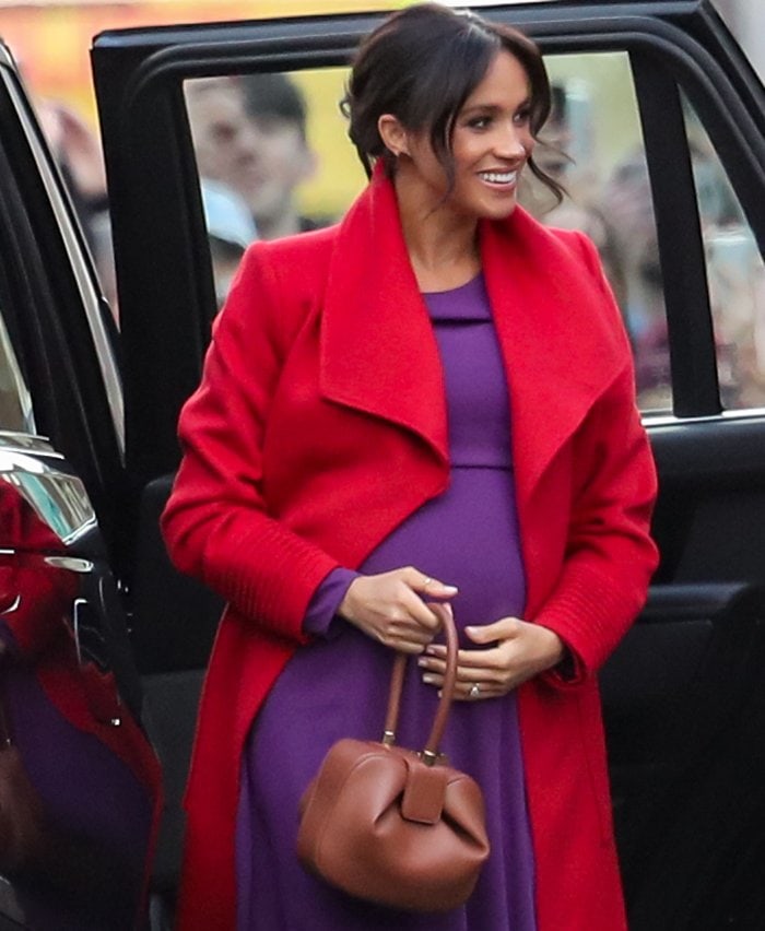 Meghan Markle revealed her due date in a Sentaler red coat paired with a purple Babaton by Artizia dress