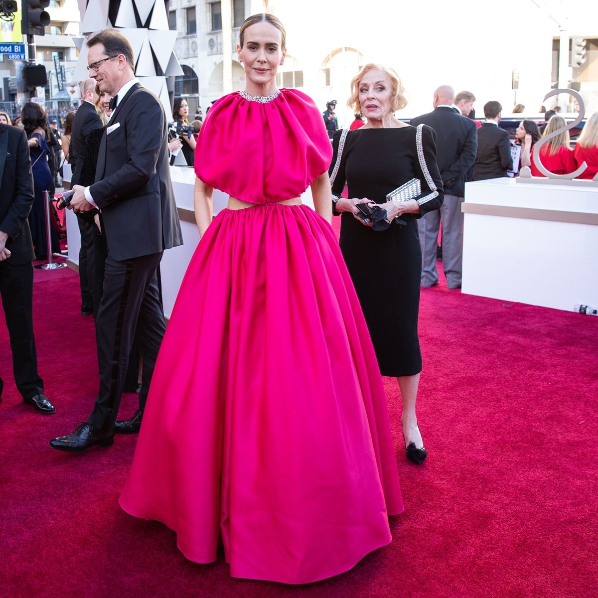 At the 91st Academy Awards, Sarah Paulson turned heads in a bold fuchsia Brandon Maxwell gown with dramatic cut-outs, while Holland Taylor exuded classic elegance in a black sheath dress with shimmering sleeve accents