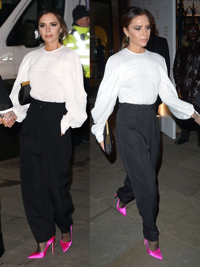 Victoria Beckham wearing a pleated long-sleeved blouse, black tapered pants, and hot-pink satin pumps all from her eponymous clothing line