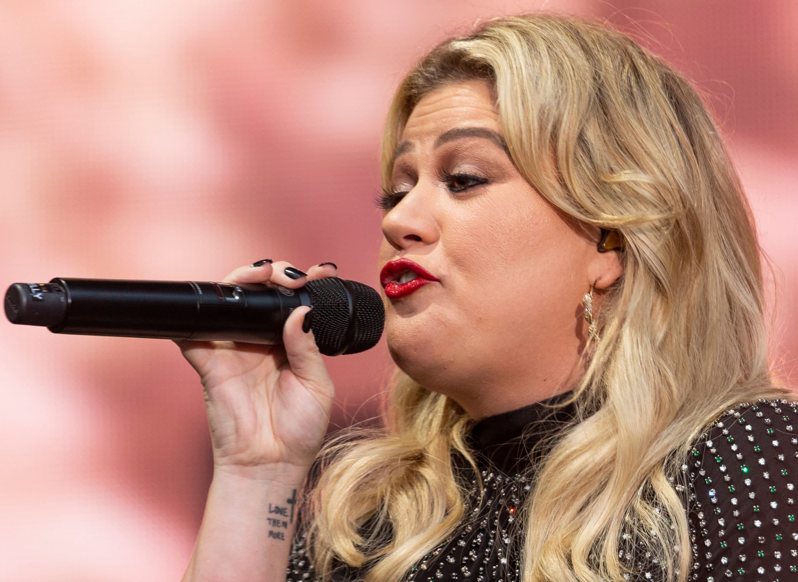 Kelly Clarkson has a cross tattoo with the words “Love Them More" inscribed on her right wrist