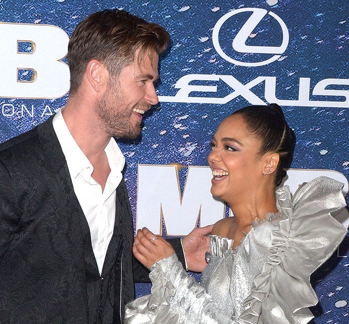 Chris Hemsworth and Tessa Thompson share a laugh on the red carpet at the Men in Black: International premiere, with Tessa stunning in her dramatic silver Rodarte gown featuring oversized ruffles and a one-shoulder design