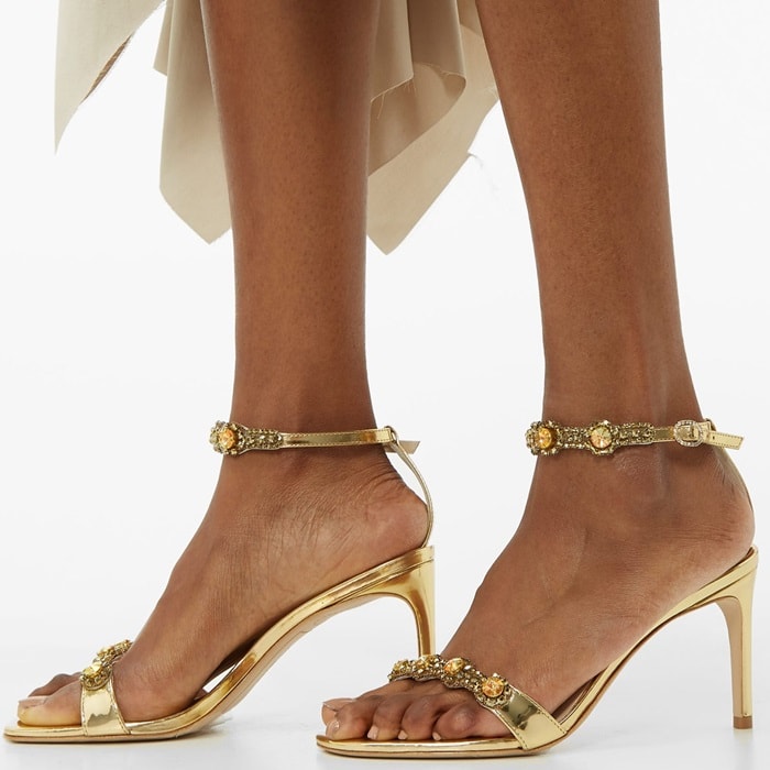 These sandals are crafted from glossy patent leather with slender toe and heel straps embellished with circular crystals, then set on a slender stiletto heel