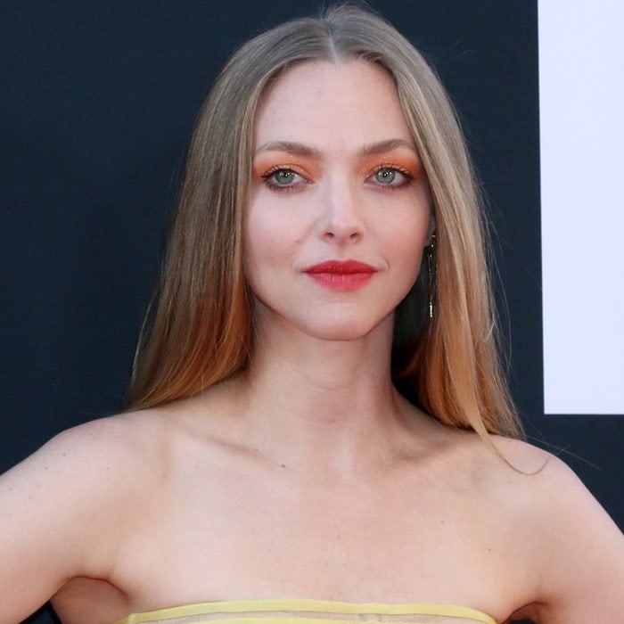 Amanda Seyfried shines with sleek, straight hair, bold orange eyeshadow, and a pop of red lipstick, perfectly complementing her radiant makeup look