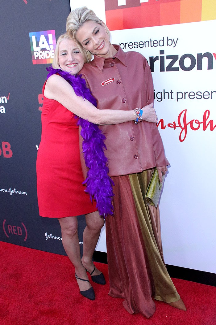 Jamie King in a maroon leather shirt being hugged by Rita Rockett