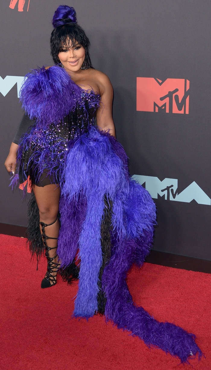 Lil' Kim makes a dramatic statement at the 2019 MTV VMAs in a feather-embellished purple-and-black mini dress by The Blonds, paired with black strappy lace-up heels