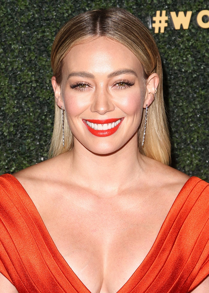 Hilary Duff complements her sleek, center-parted hairstyle with a bold red lip and radiant makeup