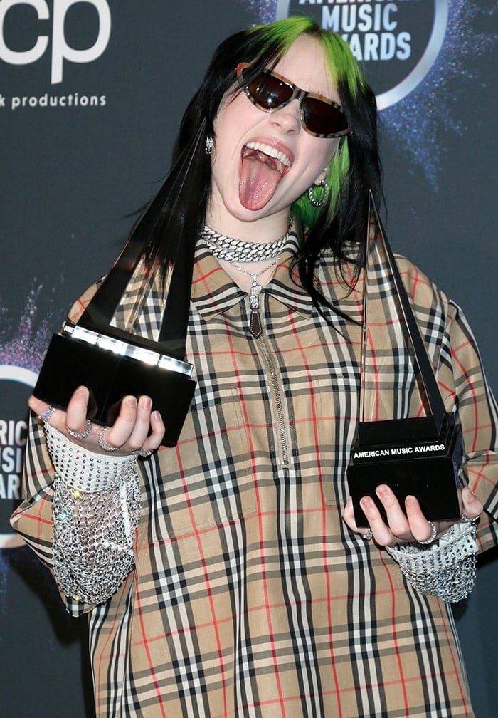 Billie Eilish shows off her two AMA trophies with a playful tongue-out pose