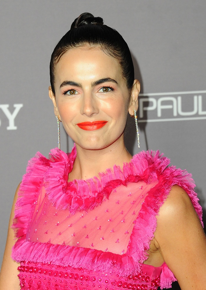 Camilla Belle pulls her hair in a bun and wears orange-red lip shade