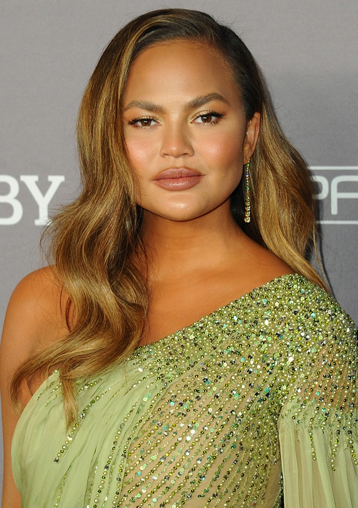 Chrissy Teigen wears her long hair in waves and sports makeup in natural palette