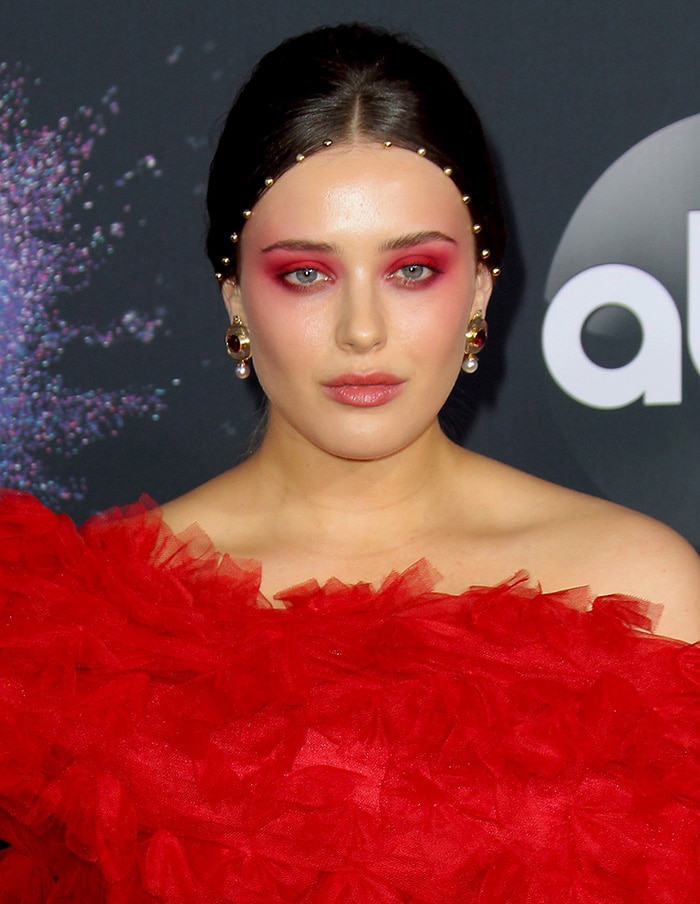 Katherine Langford wears coordinating red eye-makeup and gold studs along her hairline