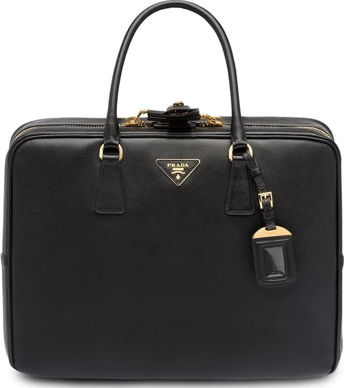 A prime example of traditional Milanese craftsmanship is this black Saffiano leather logo suitcase from Prada featuring top handles, a two-way zip fastening, a front logo plaque, gold-tone hardware, multiple interior compartments, a hanging leather tag, and a sleep mask with pouch