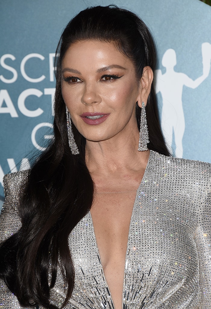 Catherine Zeta-Jones wears half-up wavy hairstyle with winged eyeliner and mauve lip shade