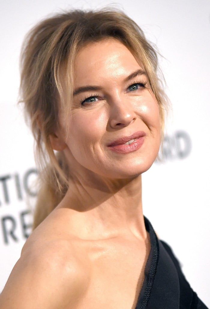 Renée Zellweger wears a messy ponytail with mascara, eyeliner, and pink lipstick