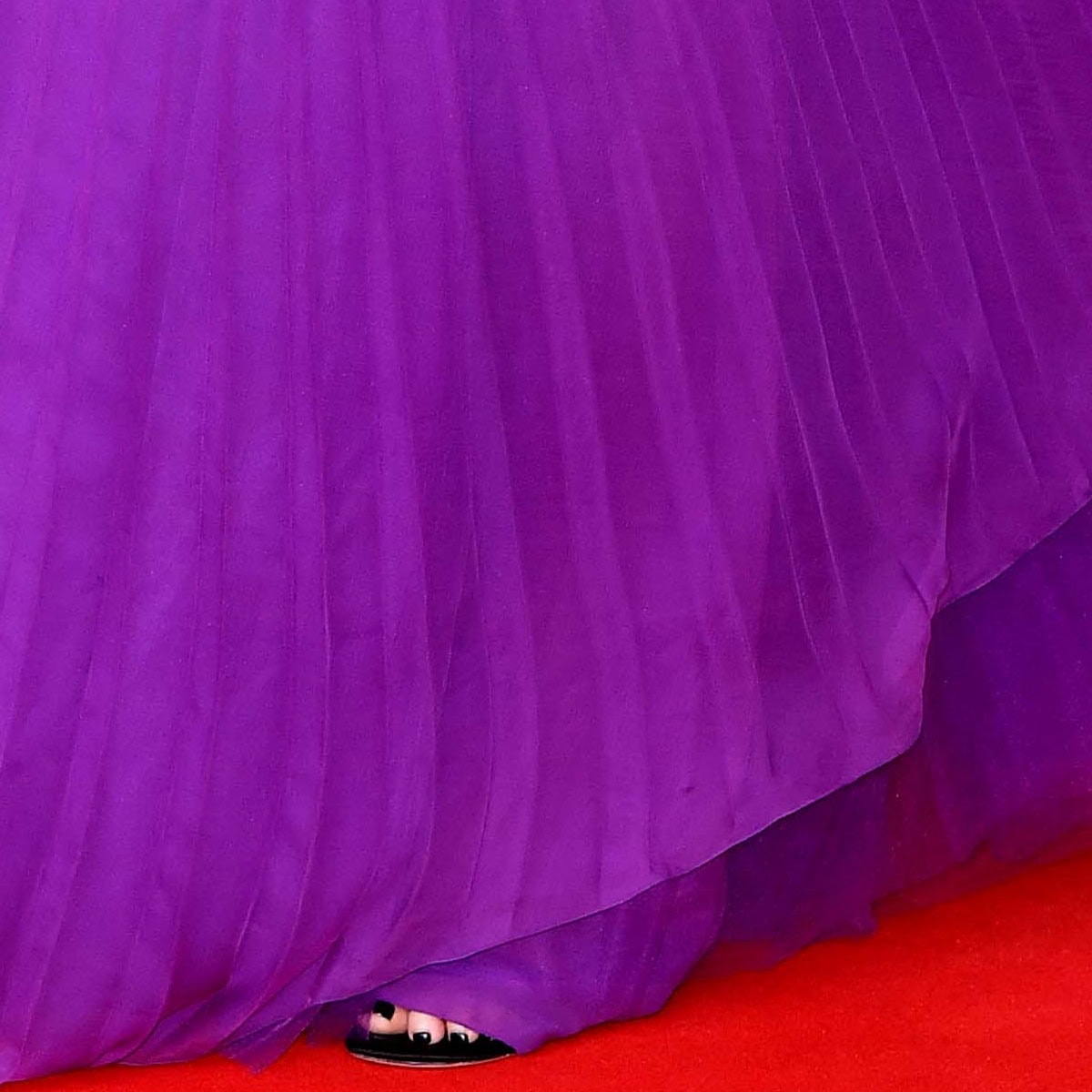 A peek beneath the pleated hem reveals Charlize Theron’s classic black open-toe heels and a polished neutral pedicure