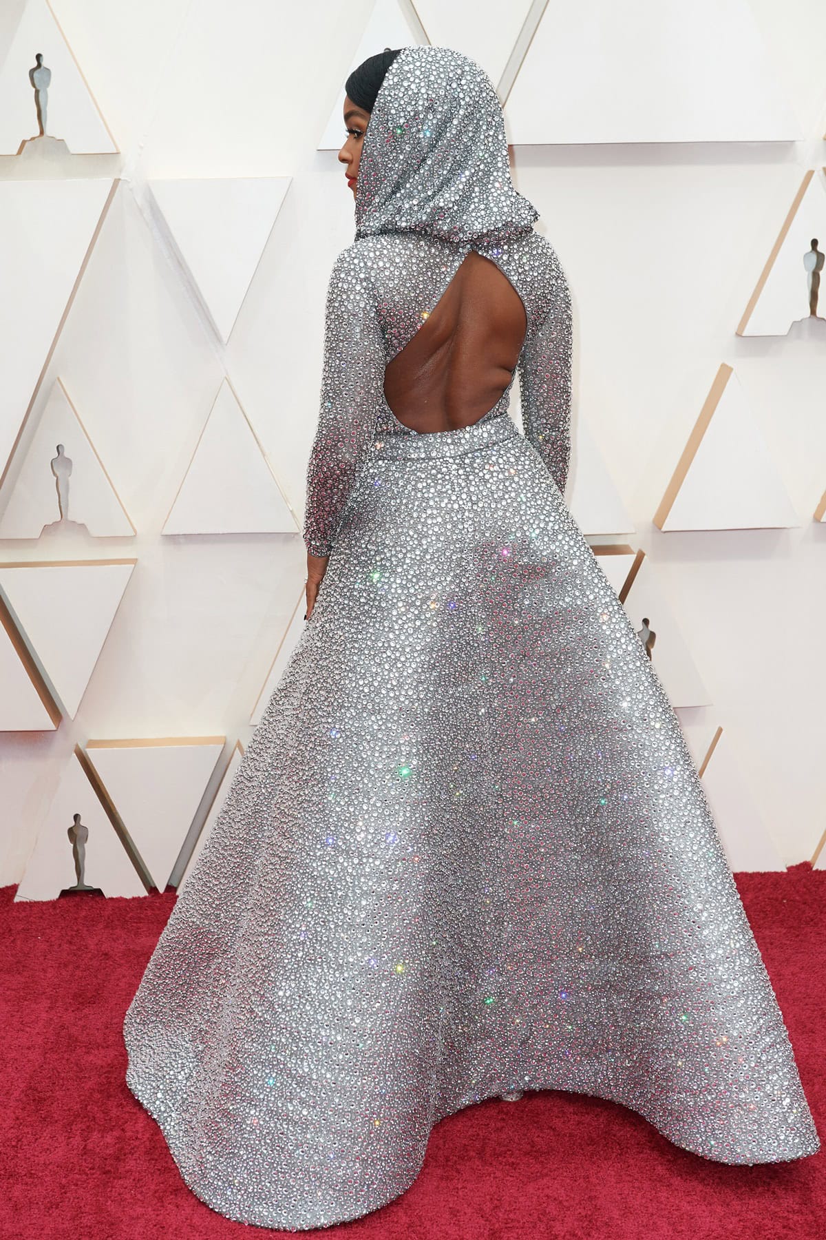 Janelle Monáe reveals the architectural drama of her crystal-embellished Ralph Lauren gown from the back, where a sculptural open cutout contrasts the full, sweeping skirt—concealing her heels beneath its luminous volume at the 2020 Oscars