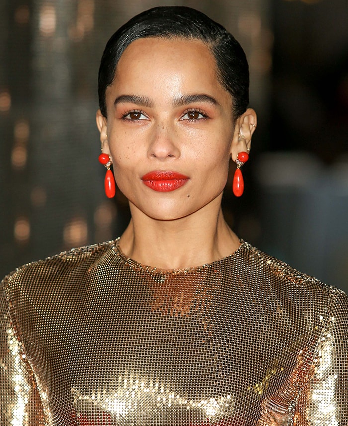 Zoe Kravitz teams her gold dress with coral earrings and lipstick