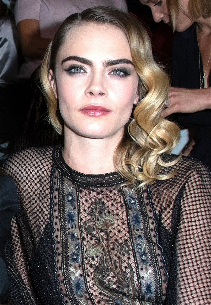 Cara Delevingne wears side-parted curls with bold brows, smoky eyeshadow and pink lipstick