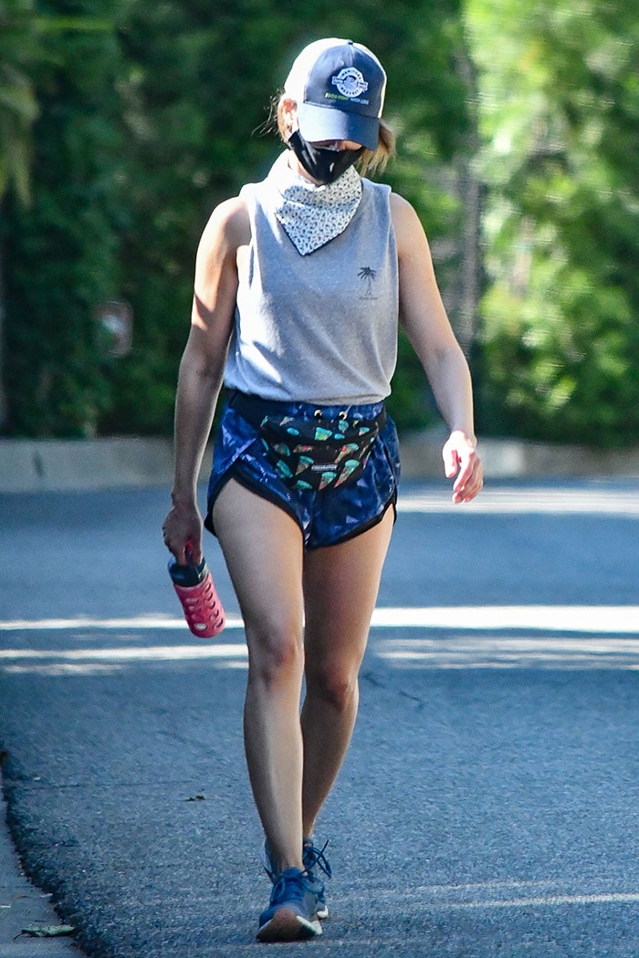 Alison Brie shows off her toned arms and legs in athletic shorts, gray sleeveless top, and running shoes