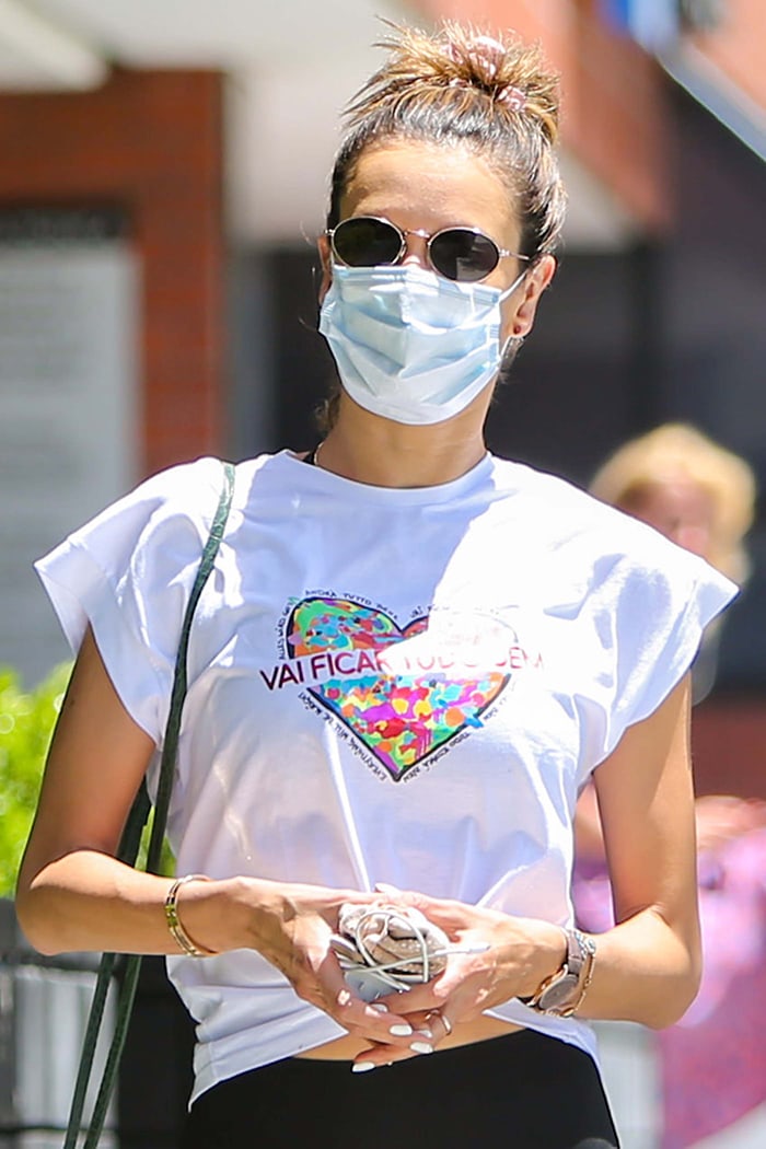 Alessandra Ambrosio keeps a low-key look with sunglasses, a facemask, and a top knot hairstyle