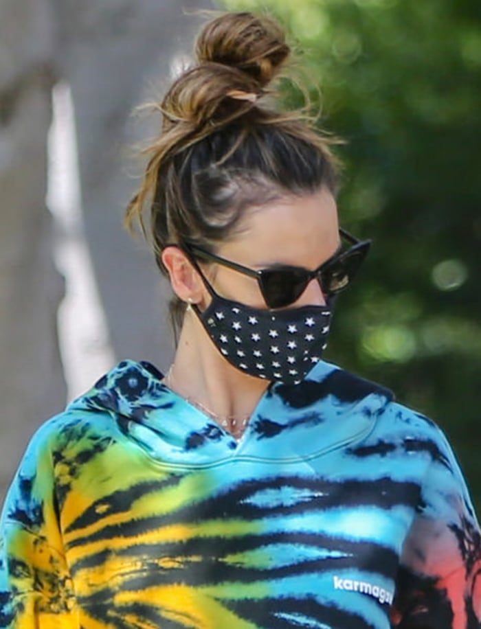 Alessandra Ambrosio styles her hair in a topknot and wears a printed face mask