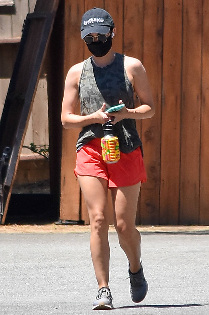 Lucy Hale wears a camo muscle tee with red shorts for hiking