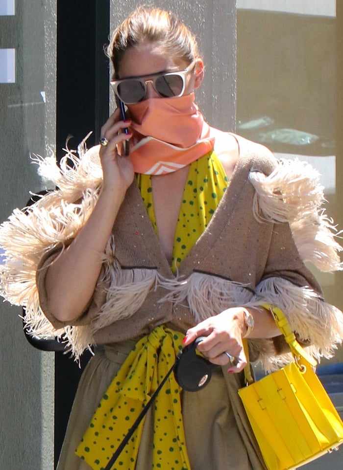 Olivia Palermo wears a pair of square sunglasses and wraps a Le Scarf No.14 scarf around her face