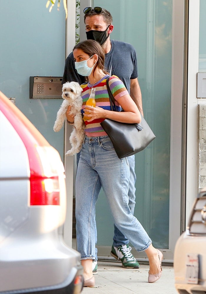 Ana de Armas steps out with Ben Affleck, cradling her adorable pup while sporting a colorful rainbow-striped top, relaxed jeans, and chic ballet flats