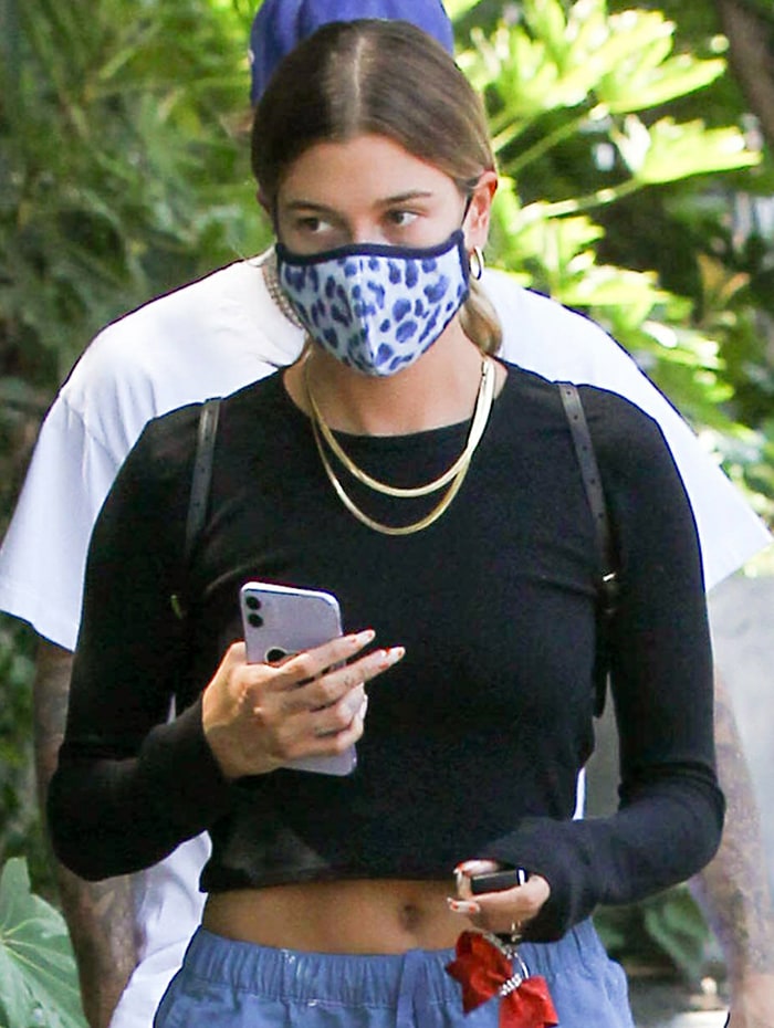 Hailey Bieber ties her hair in a ponytail and wears a leopard face mask