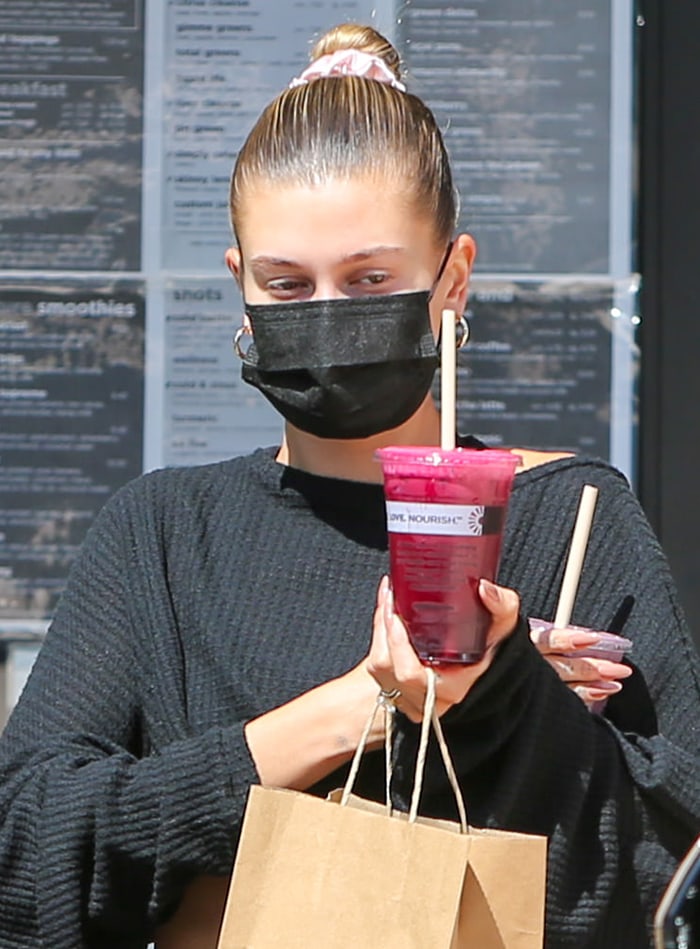 Hailey Bieber wears her hair in a sleek bun with a scrunchie