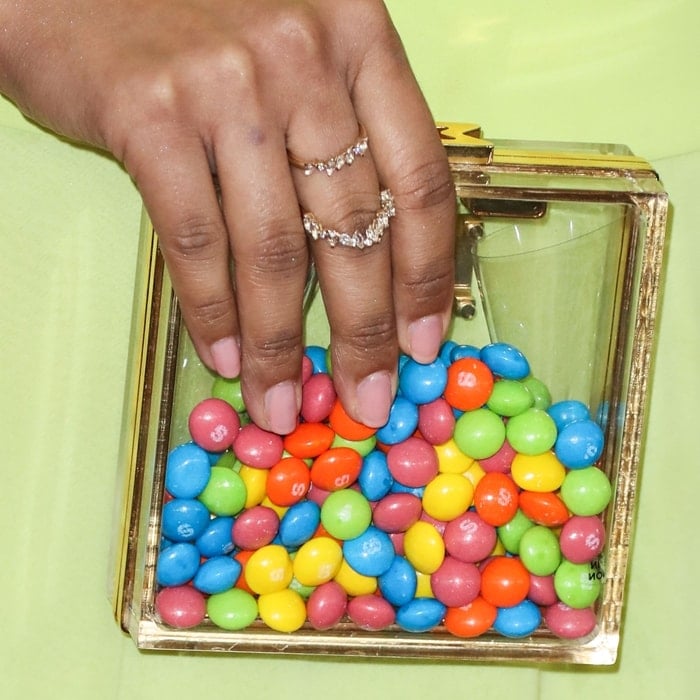 Lilly Singh adds a playful touch to her look with a clear Marzook clutch filled with colorful Skittles, paired with delicate diamond rings