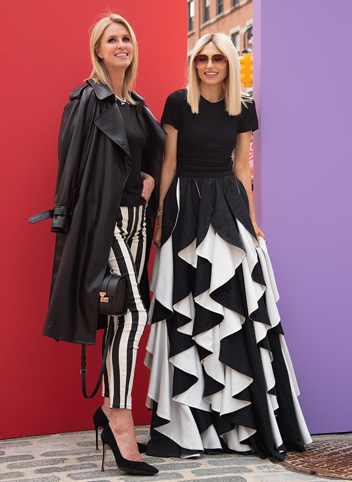 Nicky Hilton and Alice + Olivia creative director Stacey Bendet make a striking duo in coordinated black-and-white ensembles—Nicky in sleek striped skinny jeans and a leather trench, while Stacey stuns in a dramatic ruffled skirt that adds a bold touch of elegance