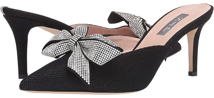 The pointed-toe black slip-on mule is constructed from luxe, shimmery fabric with a bling bow at the flirty V-vamp