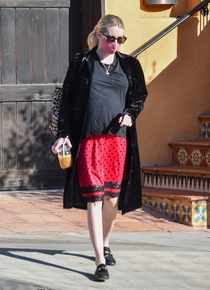 Emma Roberts' maternity look includes a loose tee, a black and red polka dot skirt, and a coat