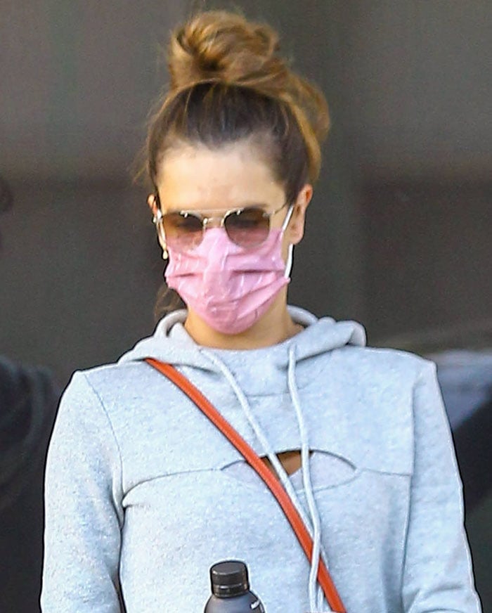 Alessandra Ambrosio wears her hair up in a bun and stays protected with a pink face mask