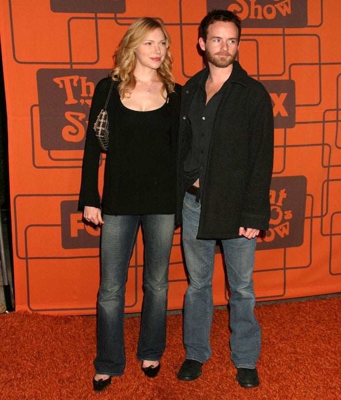 Laura Prepon, in a black top, flared jeans, and open-toe heels, poses with then-boyfriend Christopher Masterson at a That '70s Show event—highlighting their casual couple style during their relationship from 1999 to 2007