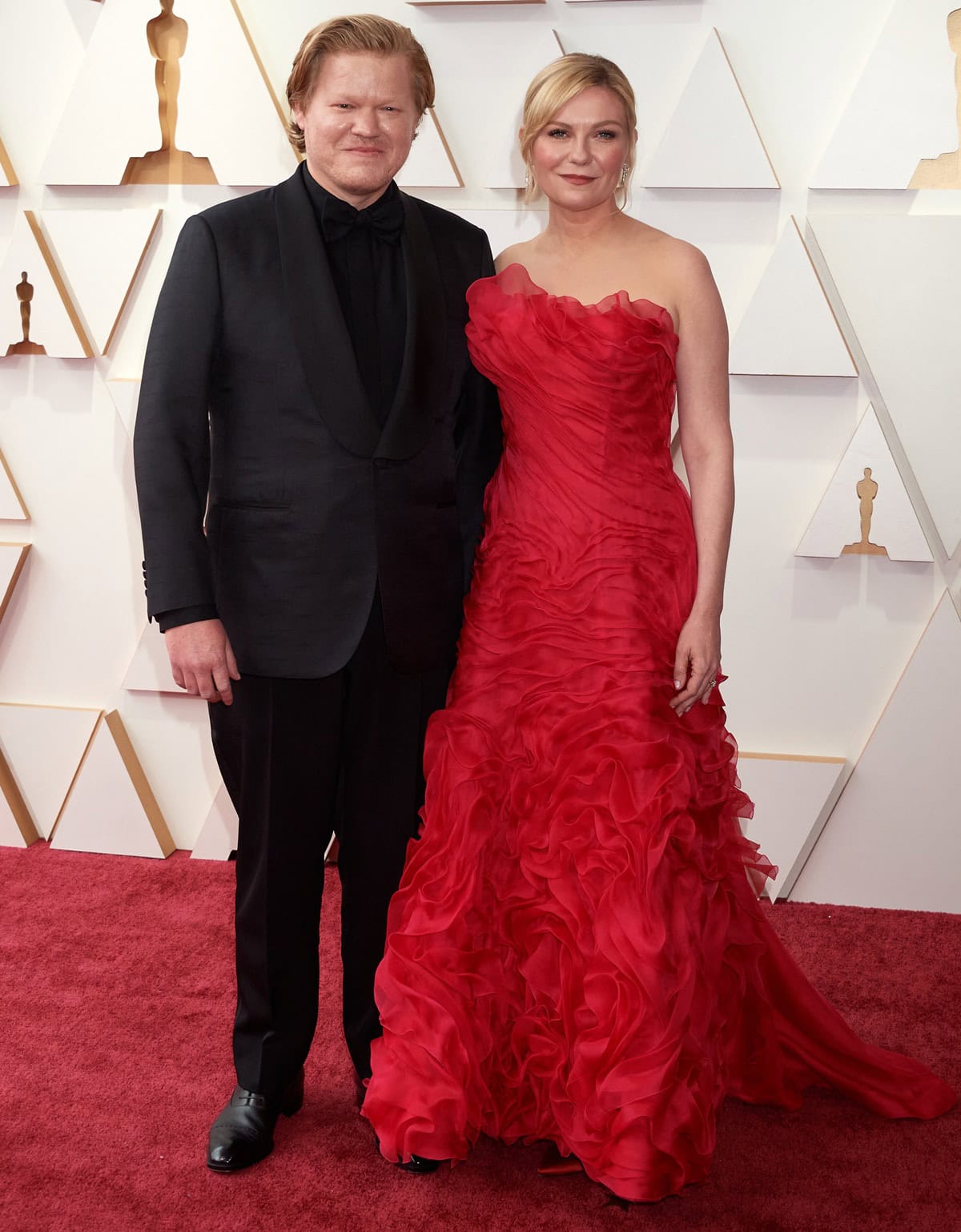 Kirsten Dunst captivates in a ruffled red vintage Christian Lacroix gown paired with delicate Roger Vivier heels, while Jesse Plemons keeps it classic in a sharply tailored black Lardini tuxedo for a perfectly balanced red-carpet moment