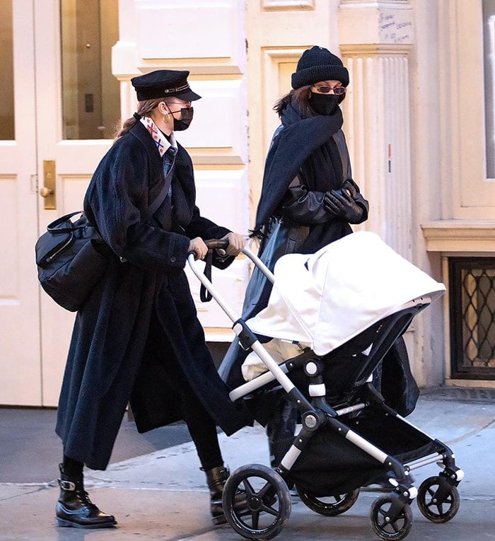 Bella Hadid complements her sister's outfit as she wears a black coat with a black scarf and a beanie