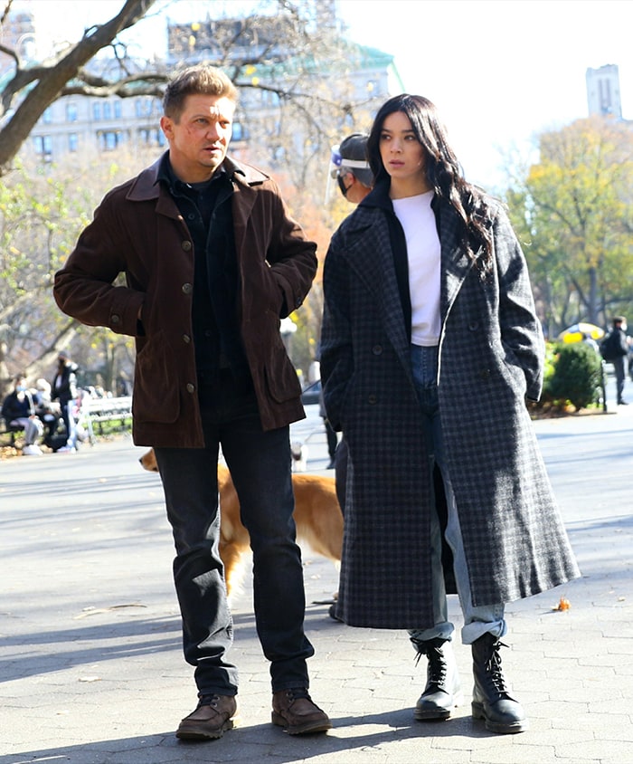 Jeremy Renner bundles up in layers of shirts and a brown jacket with black jeans and brown shoes