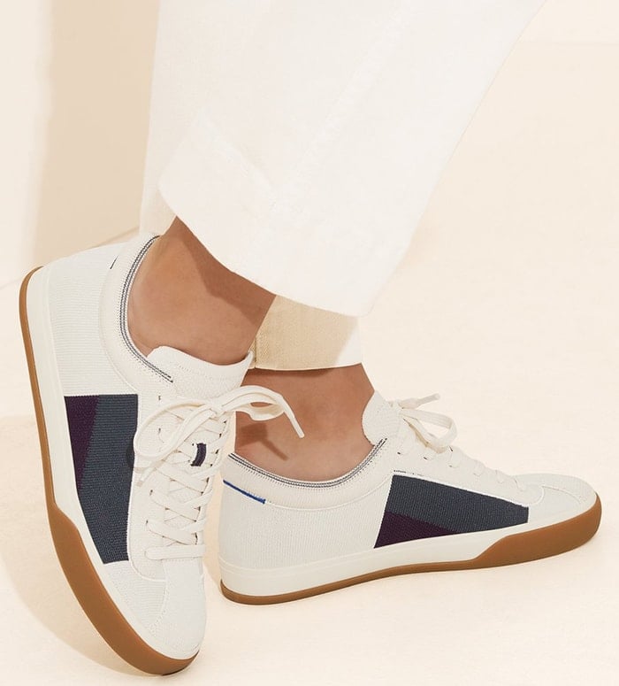 Designed for supportive structure and cloud-like comfort, this cream sneaker from Rothy’s features dark blue-grey and purple color blocking on both sides of the shoe