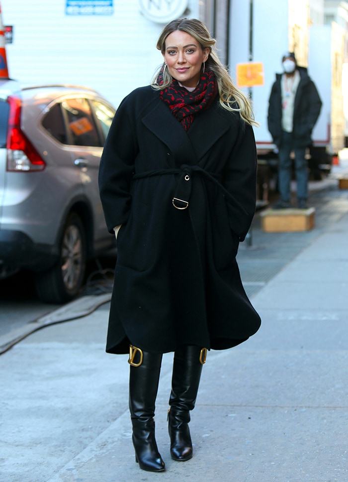 Hilary Duff covers her baby bump in a black trench coat and red-and-black printed scarf