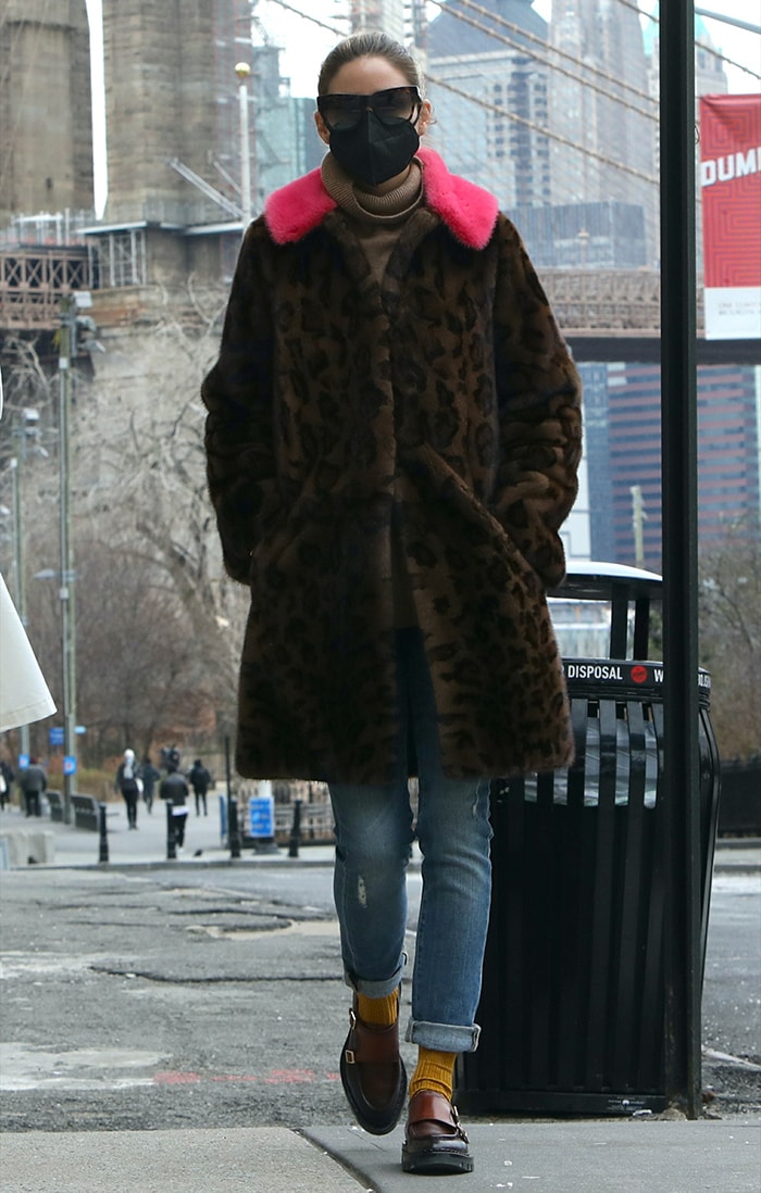 Olivia Palermo wears a leopard coat with a pink fur trim over a brown sweater and a pair of jeans