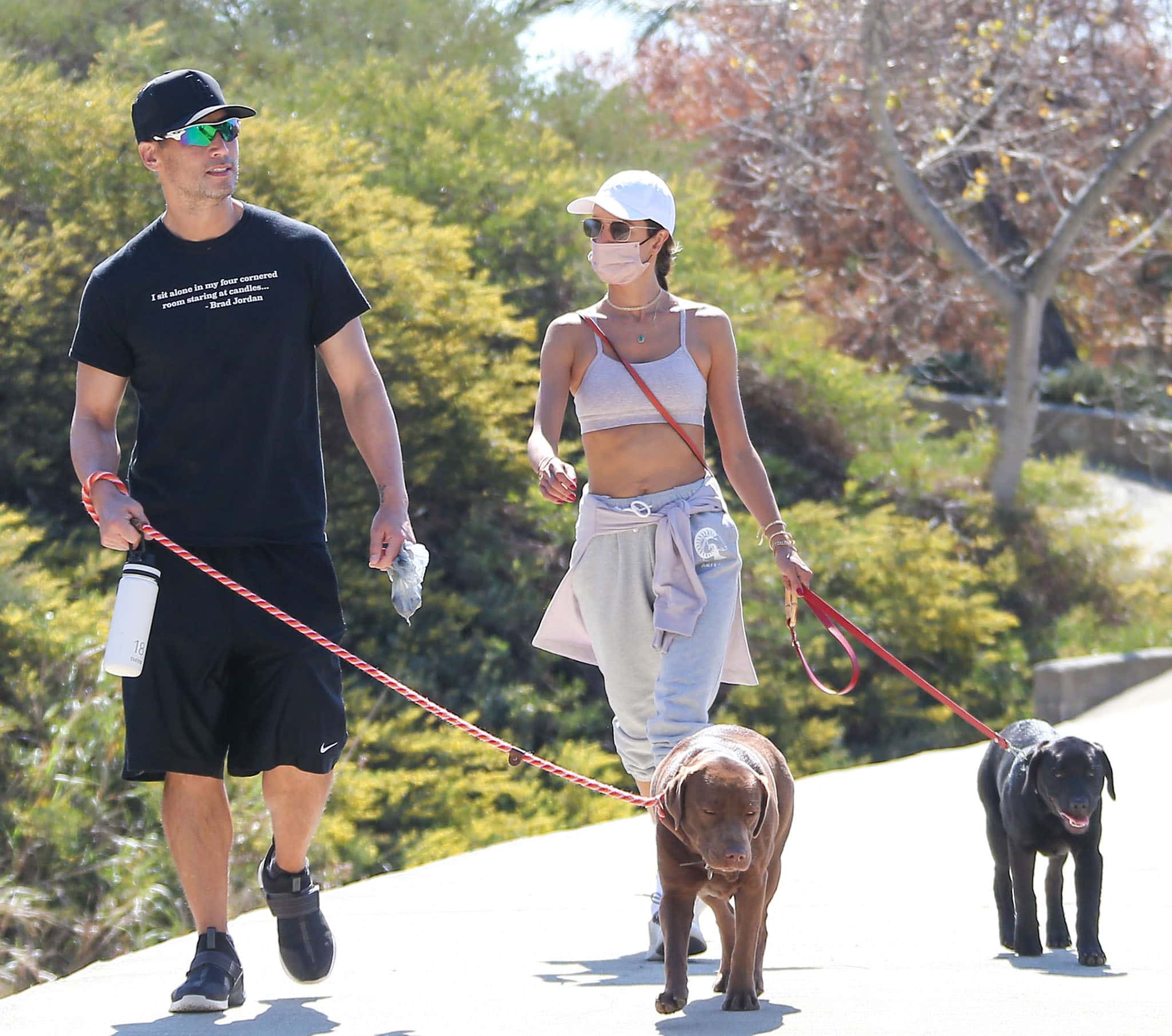 Alessandra Ambrosio's male companion wears a black tee with black basketball shorts, cap, and sneakers