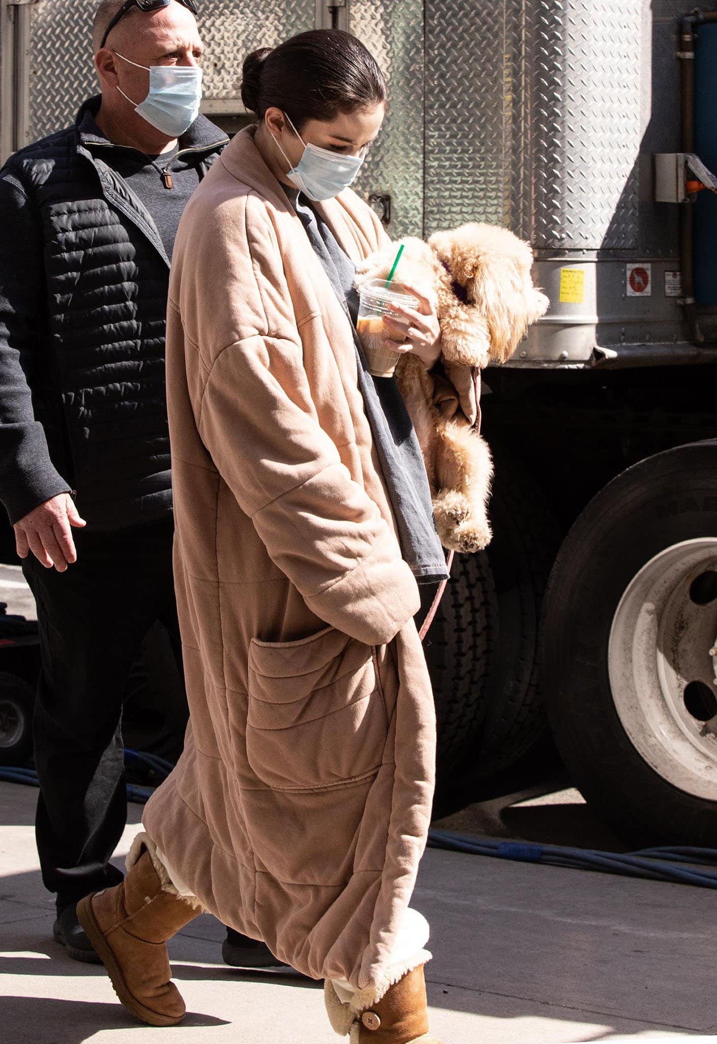 Selena Gomez looks cozy in Free People duvet coat and Ugg boots while carrying her fluffy dog, Daisy, on the set