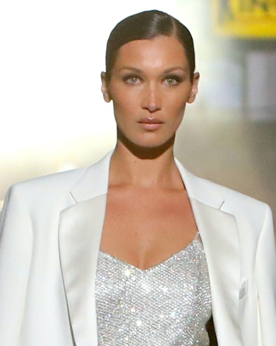 Bella Hadid styles her locks in a sleek ponytail with a deep side part and wears neutral makeup with smokey eye shadow