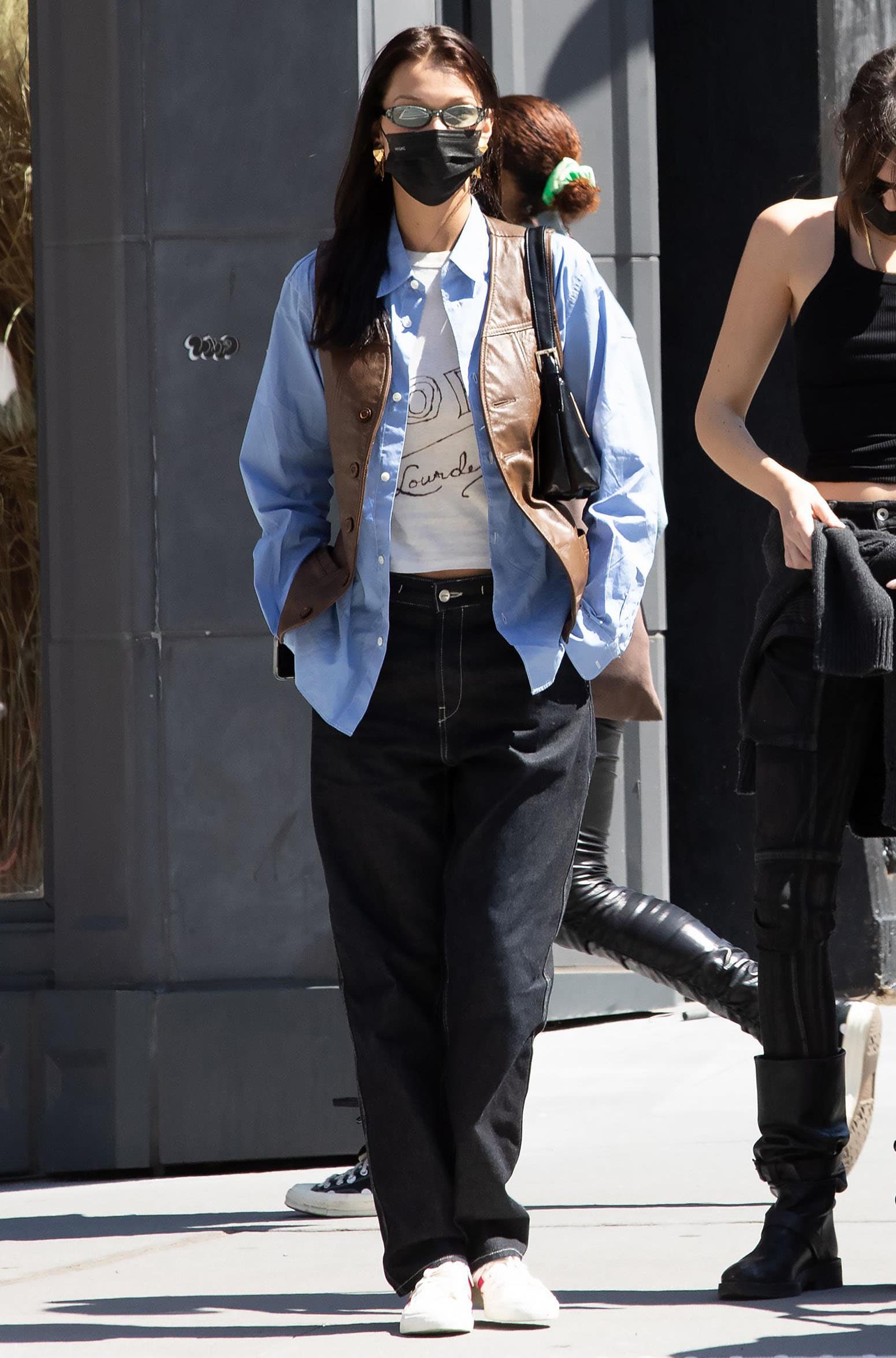 Bella Hadid goes the '90s route in crop tee and baggy jeans layered with a brown leather vest and blue button-down shirt