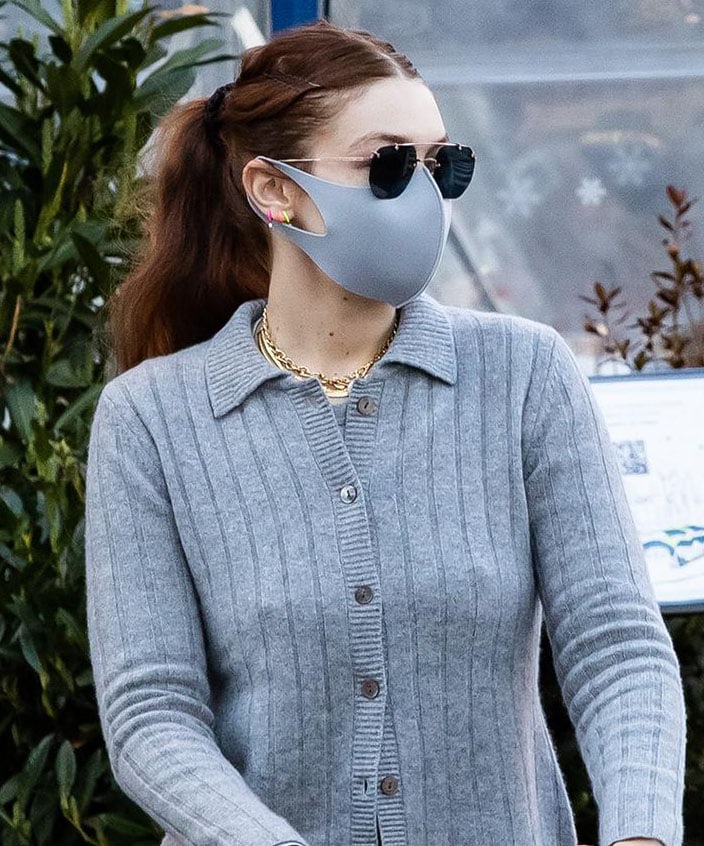Gigi Hadid styles her long hair in a center-parted wavy ponytail and stays low profile with a Lapcos face mask and Tejesta sunnies